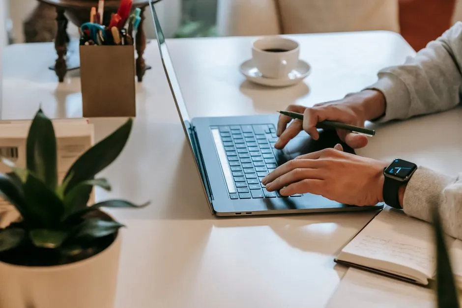 Freelancer working on a laptop with a notepad and coffee cup, illustrative stock photo