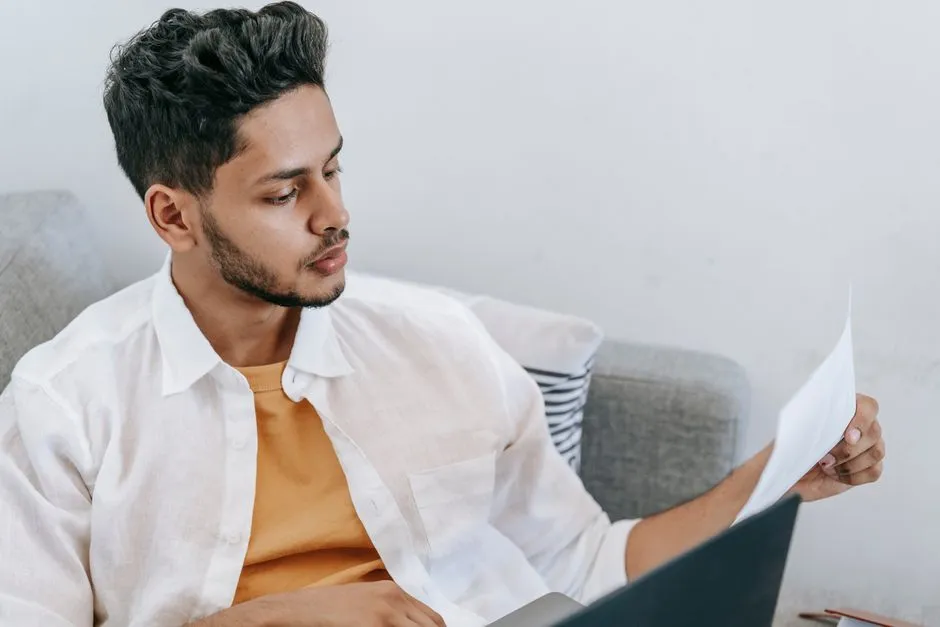 Person carefully reading a document alongside a laptop before agreeing to a job offer, illustrative stock photo